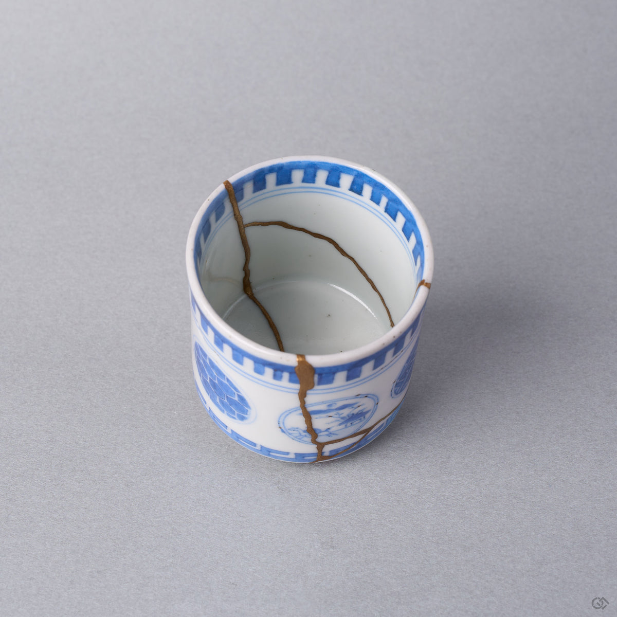 Kintsugi sake cup interior at an angle, natural urushi and 24K gold lines descending the white wall of the Ko-Imari porcelain toward the well.