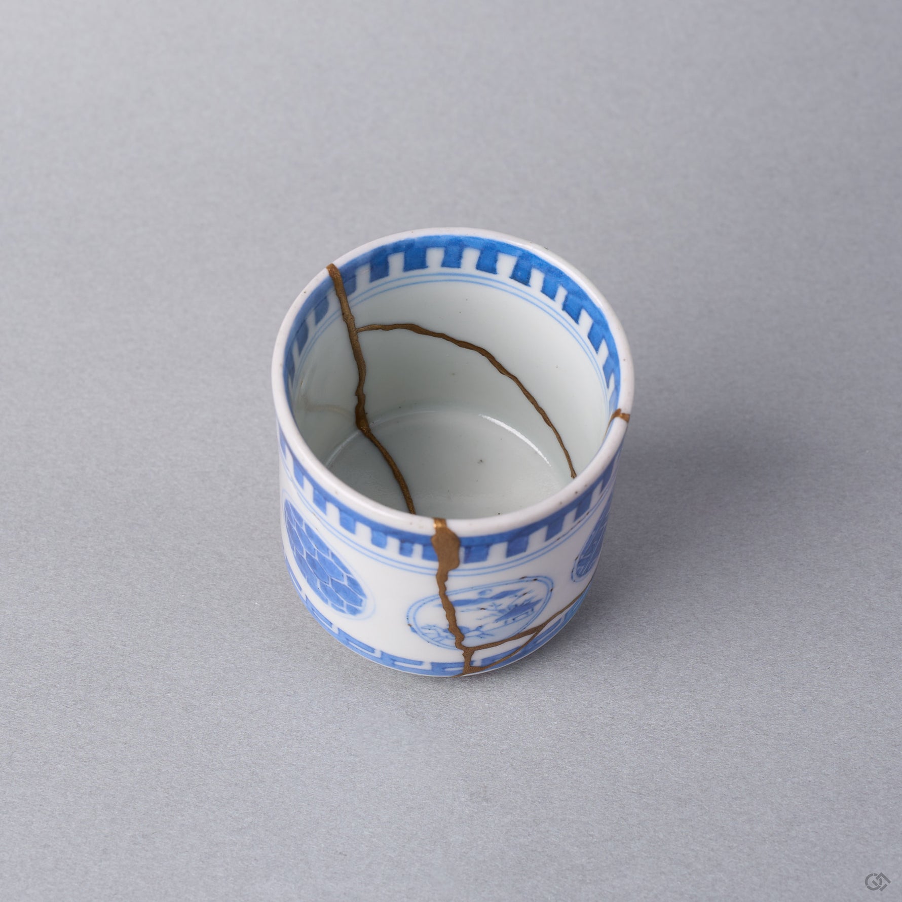 Kintsugi sake cup interior at an angle, natural urushi and 24K gold lines descending the white wall of the Ko-Imari porcelain toward the well.