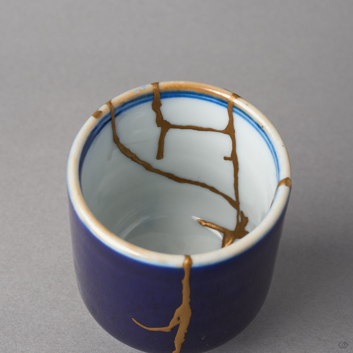 Kintsugi sake cup in lapis-blue Ko-Imari porcelain, rejoined with natural urushi, 24K gold seams branching across the white well, interior close-up 1.