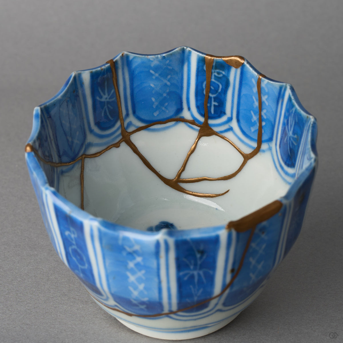 Kintsugi sake cup in Ko-Imari porcelain, rejoined with natural urushi, 24K gold seams crossing the white well and forking near the center, interior view.