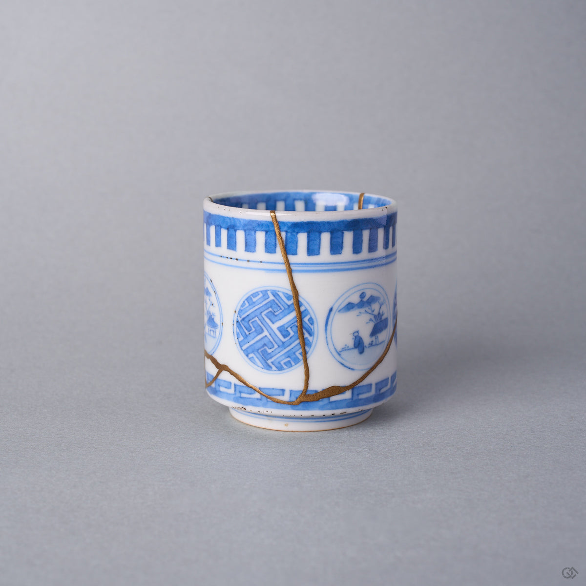 Kintsugi sake cup side view, a natural urushi and 24K gold seam descending through the sayagata window of the Ko-Imari porcelain and branching at the lower cup.