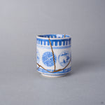 Kintsugi sake cup side view, a natural urushi and 24K gold seam descending through the sayagata window of the Ko-Imari porcelain and branching at the lower cup.