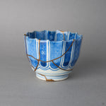 Kintsugi sake cup in Ko-Imari porcelain with a scalloped rim, rejoined with natural urushi, one 24K gold seam running from rim to foot, side view.