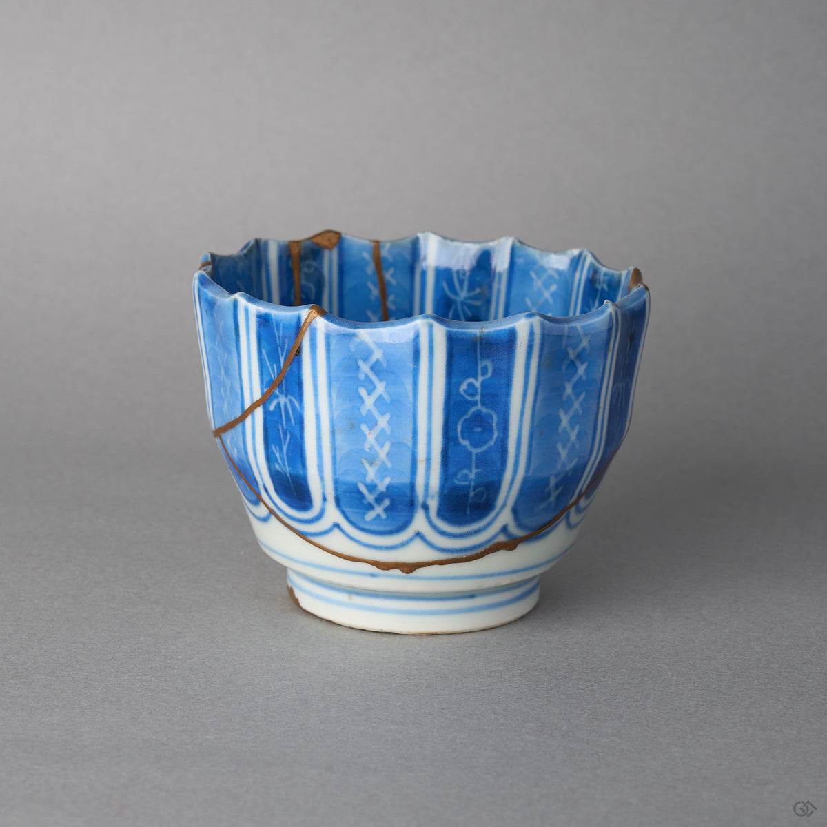 Kintsugi sake cup in blue-and-white Ko-Imari porcelain, rejoined with natural urushi, a 24K gold seam circling the base below the columns, side view.