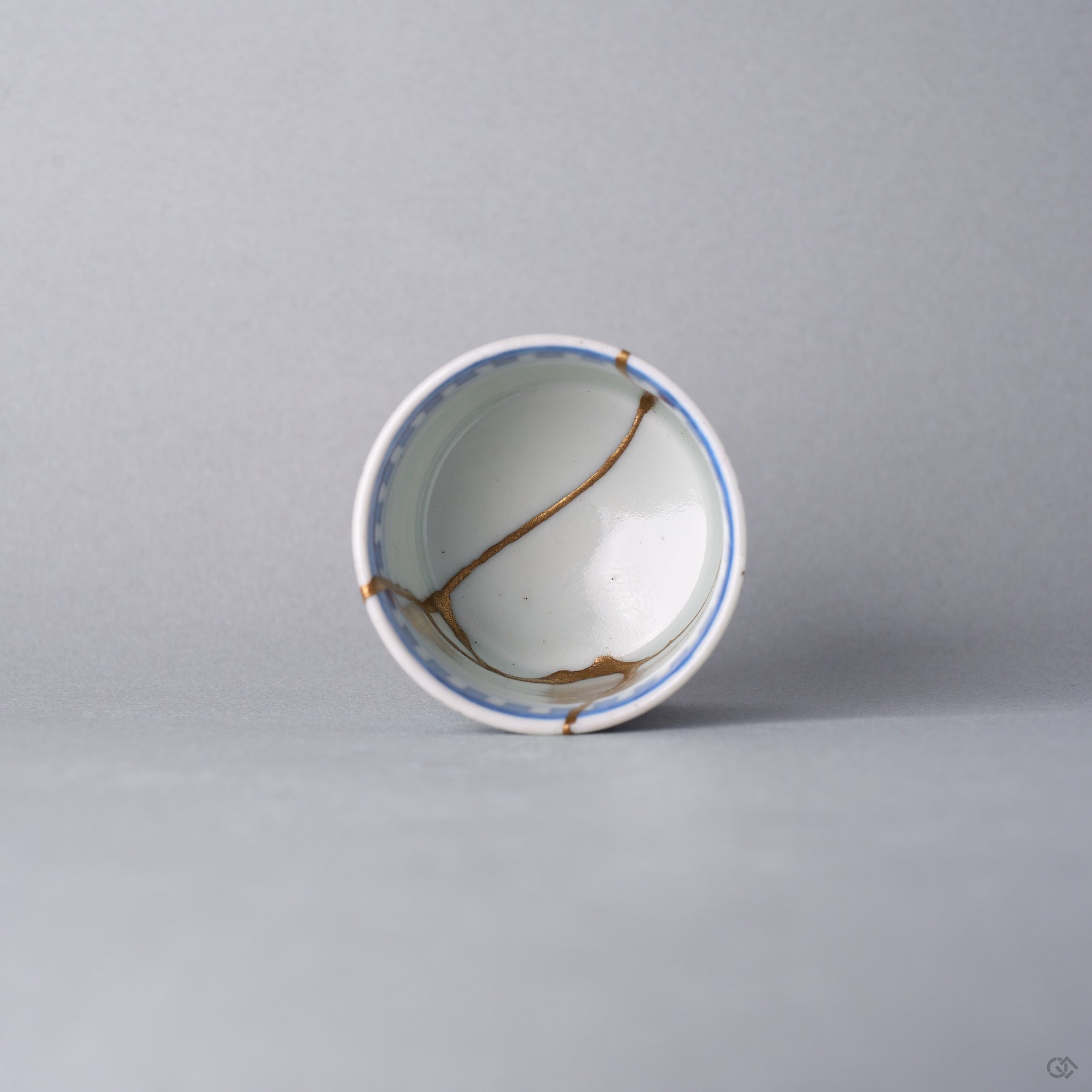 Kintsugi sake cup seen from above, a natural urushi and 24K gold line crossing the white interior of the Ko-Imari porcelain toward the well.