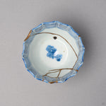 Kintsugi sake cup in Ko-Imari porcelain from above, rejoined with natural urushi, 24K gold seams passing beside the blue blossom in the center, top view.