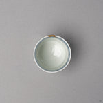 Kintsugi sake cup in Ko-Imari porcelain from above, the white well ringed by a lattice band, one short 24K gold cap over the natural urushi rim, top view.