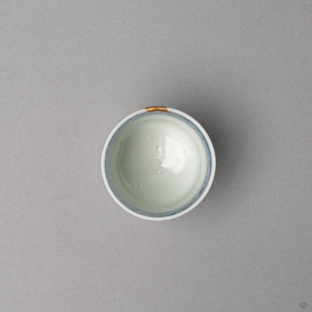 Kintsugi sake cup in Ko-Imari porcelain from above, the white well ringed by a lattice band, one short 24K gold cap over the natural urushi rim, top view.