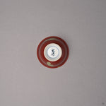 Kintsugi sake cup in red Kyoto ware porcelain seen from below, the white foot with a blue kiln mark and urushi-painted bird tips at the edge, bottom view.