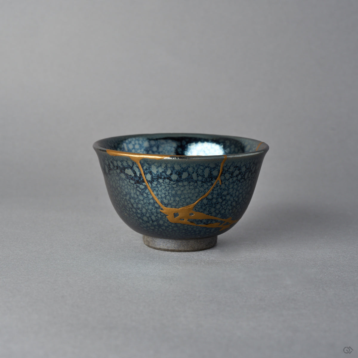 Kintsugi sake cup in Kyoto ware tenmoku glaze, rejoined with natural urushi, one 24K gold seam dividing from the rim and meeting above the foot, front.
