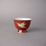Kintsugi sake cup in red Kyoto ware porcelain restored with natural urushi, the second hummingbird in flight painted in pale urushi, side view.