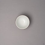 Kintsugi sake cup in Kyoto ware porcelain seen from above, the white interior and dark rim line visible, restored with natural urushi, top view.