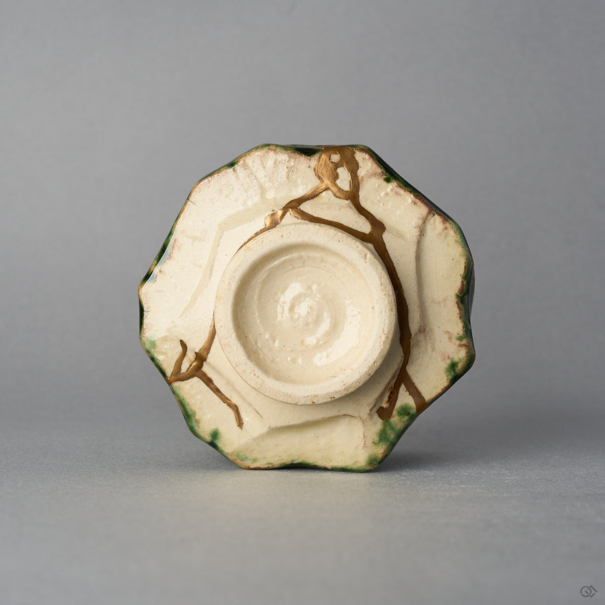 Kintsugi sake cup in Oribe ware seen from below, natural urushi and 24K gold seams crossing the unglazed base toward the foot ring, bottom view.