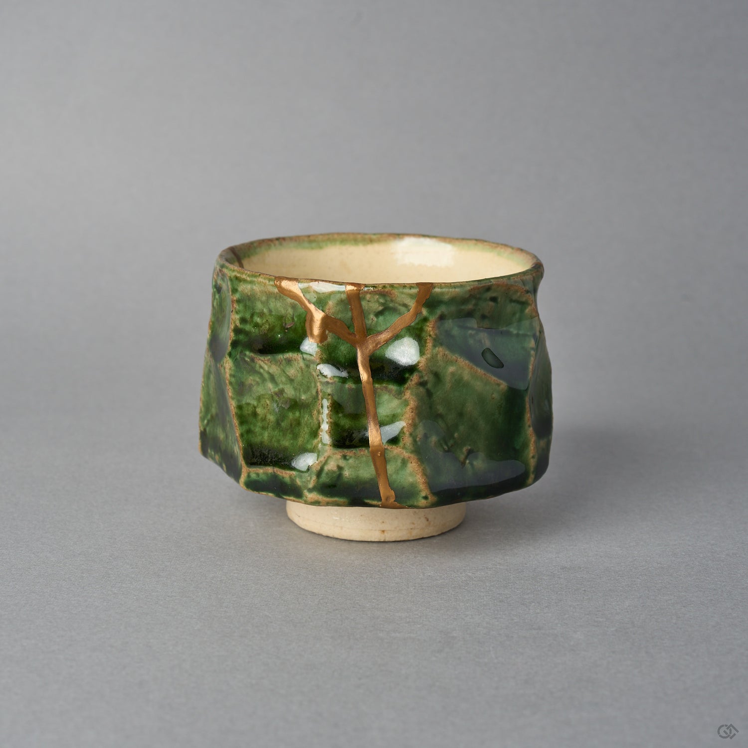 Kintsugi sake cup in faceted Oribe green pottery, a natural urushi and 24K gold seam forking below the rim and descending the facet to the foot, front view.