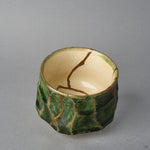 Kintsugi sake cup in Oribe ware tilted to show the ivory well, a natural urushi and 24K gold line curving from the rim down to the interior center.