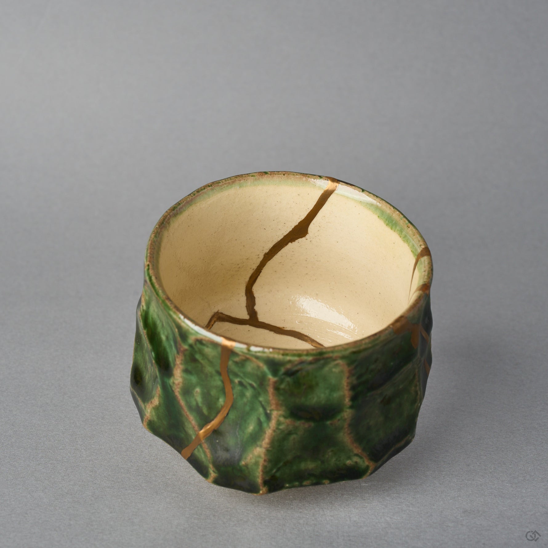 Kintsugi sake cup in Oribe ware tilted to show the ivory well, a natural urushi and 24K gold line curving from the rim down to the interior center.