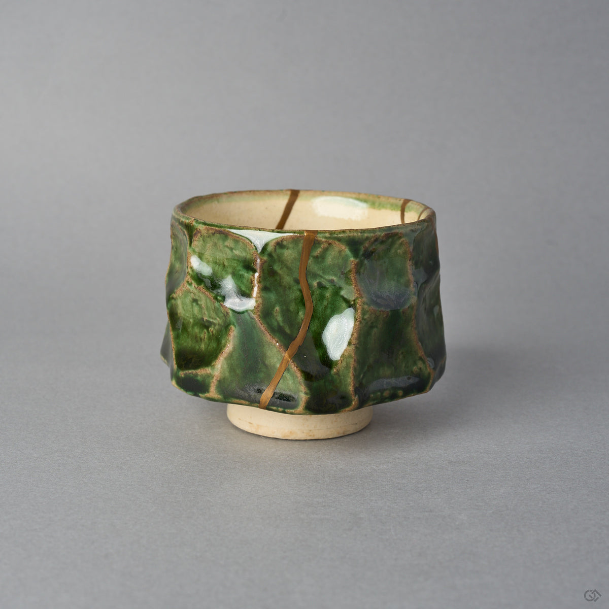 Kintsugi sake cup in Oribe green pottery seen from the side, one natural urushi and 24K gold line running straight down the faceted wall from rim to foot.