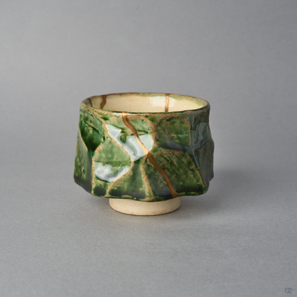 Kintsugi sake cup in Oribe ware seen from the side, a natural urushi and 24K gold seam slanting across a milky pool of glaze on the copper-green facets.