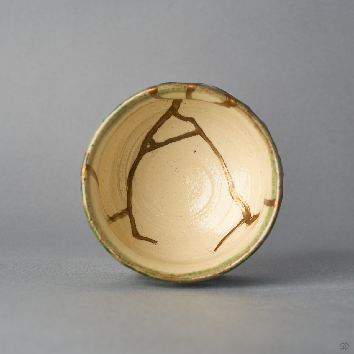 Kintsugi sake cup in Oribe ware seen from directly above, natural urushi and 24K gold lines branching across the ivory well within the green rim, top view.