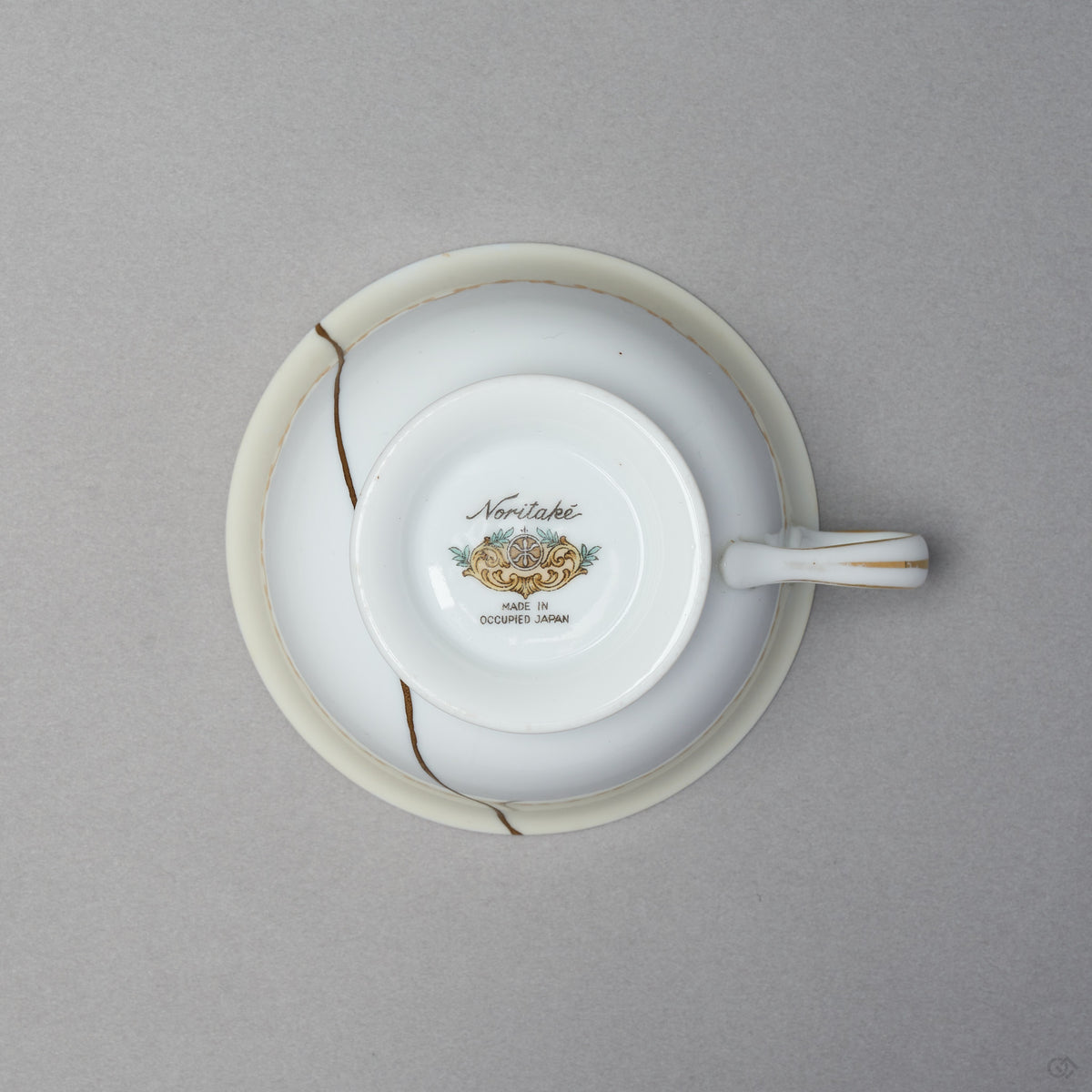 Kintsugi tea cup in Early Noritake porcelain, seen from below: the backstamp sits on the foot and the 24K gold urushi seam crosses the body beside it.