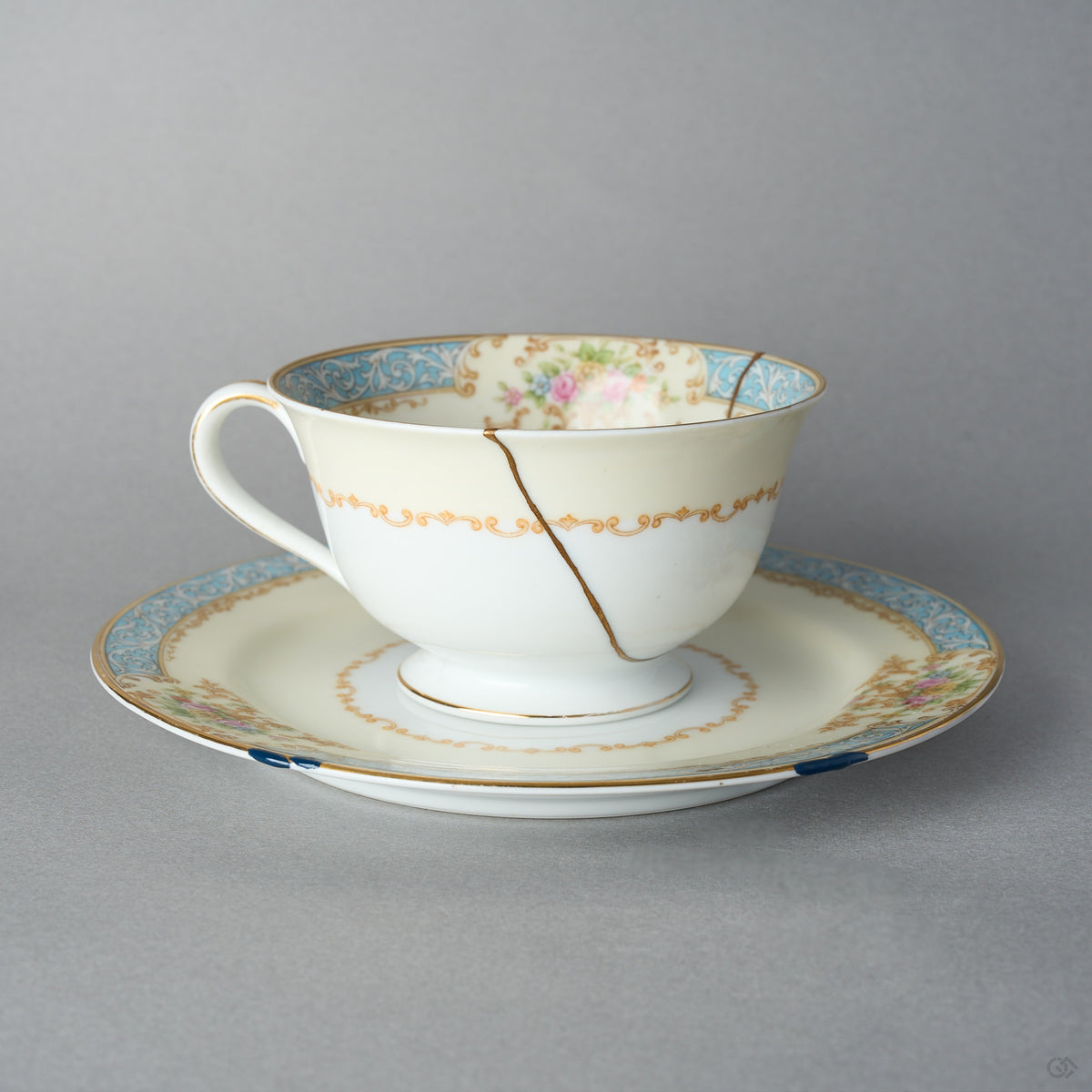 Kintsugi tea cup and saucer in Early Noritake porcelain, front view: one 24K gold seam in natural urushi runs from the rim across the scroll band.