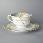 Kintsugi tea cup and saucer in Early Noritake porcelain, front view: one 24K gold seam in natural urushi runs from the rim across the scroll band.