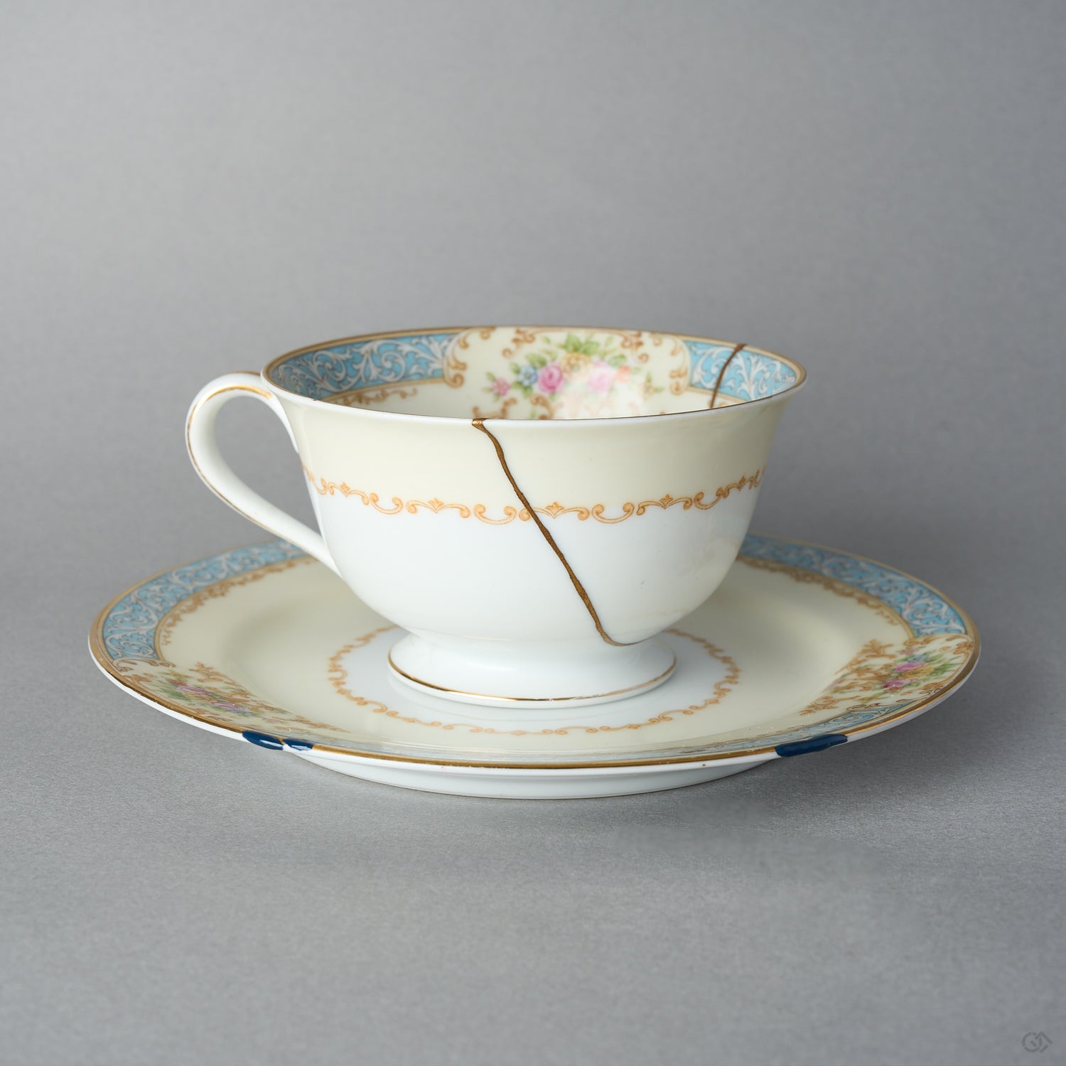 Kintsugi tea cup and saucer in Early Noritake porcelain, front view: one 24K gold seam in natural urushi runs from the rim across the scroll band.