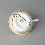 Kintsugi tea cup in Early Noritake porcelain seen from below, natural urushi and 24K gold seams crossing the base and foot ring, bottom view.