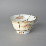 Kintsugi tea cup in cream Early Noritake porcelain, three natural urushi and 24K gold lines descending past the painted roses to meet at the foot, front view.