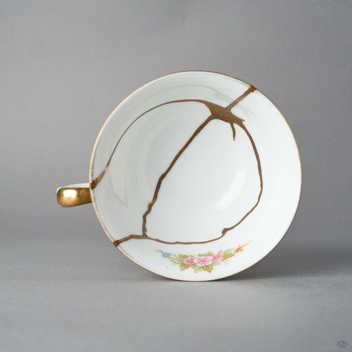 Kintsugi tea cup in Early Noritake porcelain seen from directly above, natural urushi and 24K gold seams gathering into a star in the white well, top view.