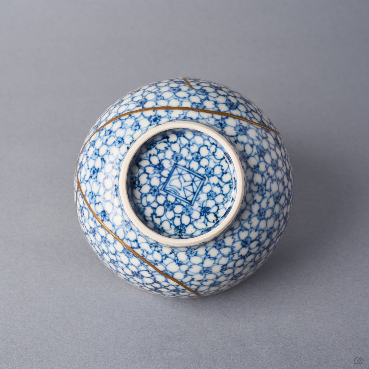 Kintsugi tea cup base with blossoms continuing under the foot around a blue kiln mark, urushi and 24K gold seams beside the foot ring.