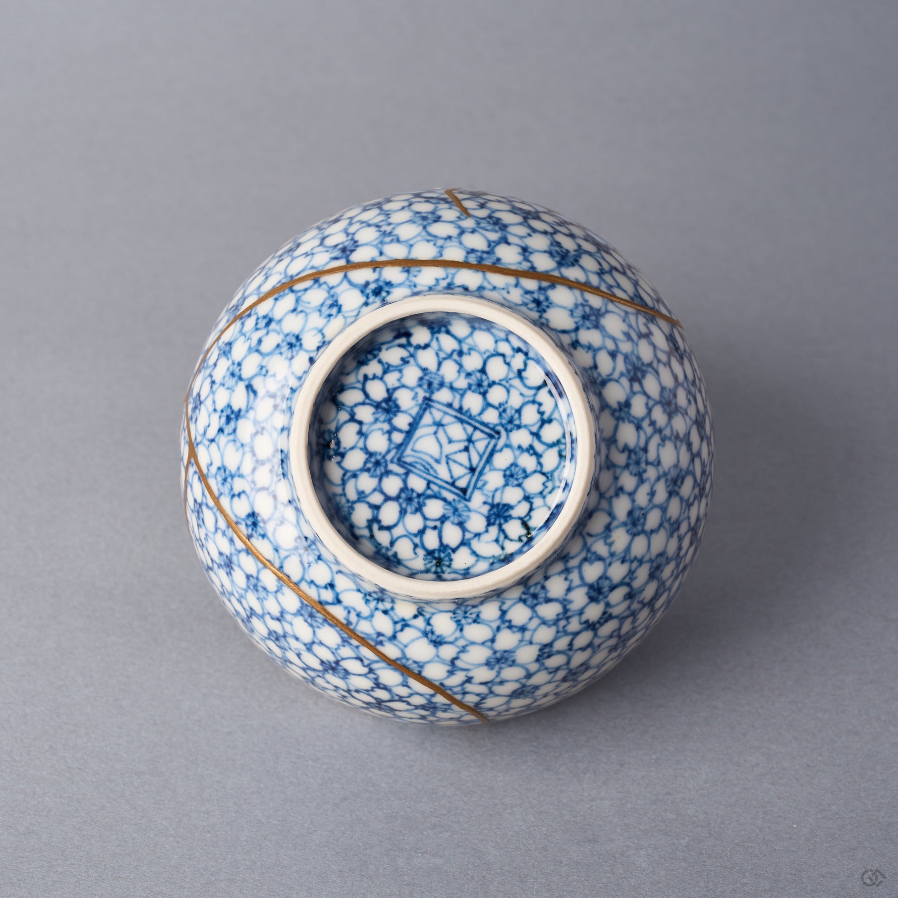 Kintsugi tea cup base with blossoms continuing under the foot around a blue kiln mark, urushi and 24K gold seams beside the foot ring.