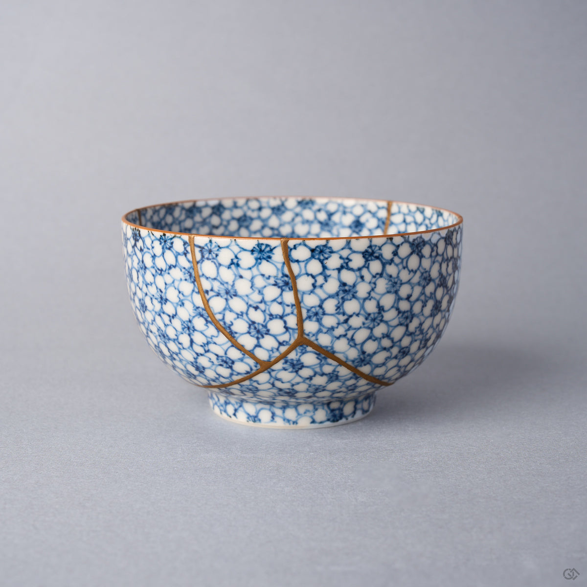Kintsugi tea cup in Kyoto ware: a branching seam of natural urushi and 24K gold descends the packed cherry-blossom porcelain, front view.