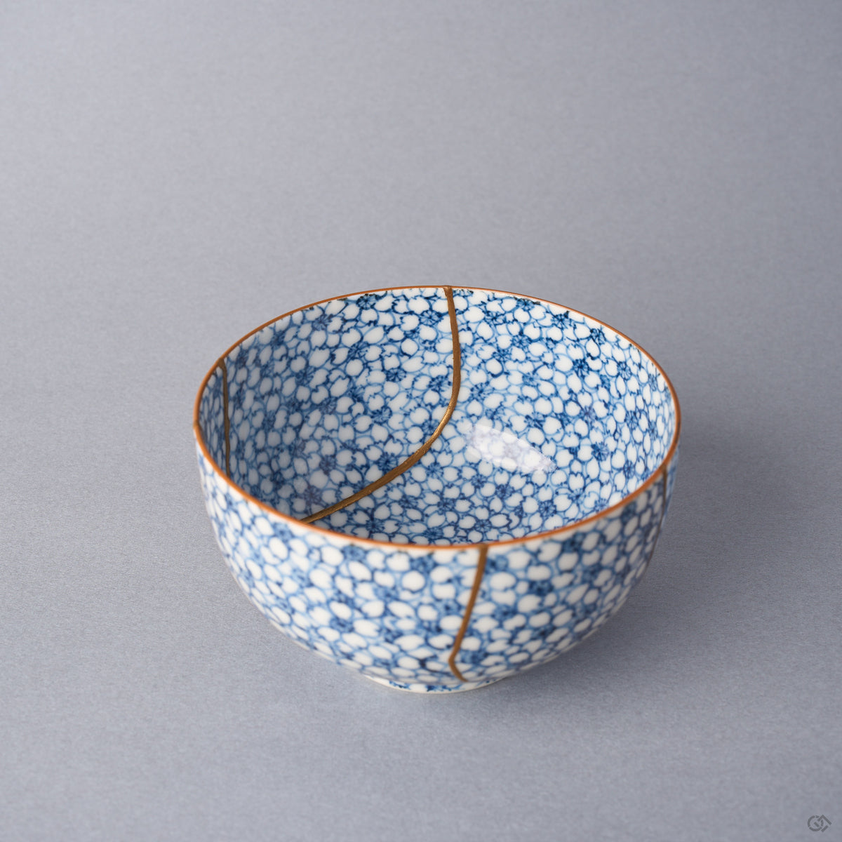 Kintsugi tea cup interior with an urushi and 24K gold seam dividing above the well of the blossom-covered porcelain.