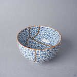Kintsugi tea cup interior where a long urushi and 24K gold seam sweeps across the cherry-blossom porcelain and forks toward the rim.