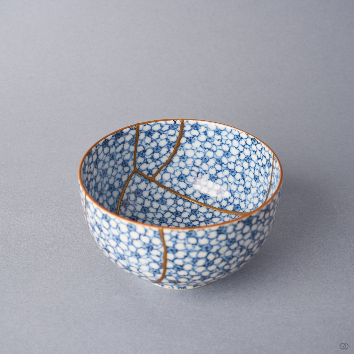 Kintsugi tea cup interior where a long urushi and 24K gold seam sweeps across the cherry-blossom porcelain and forks toward the rim.