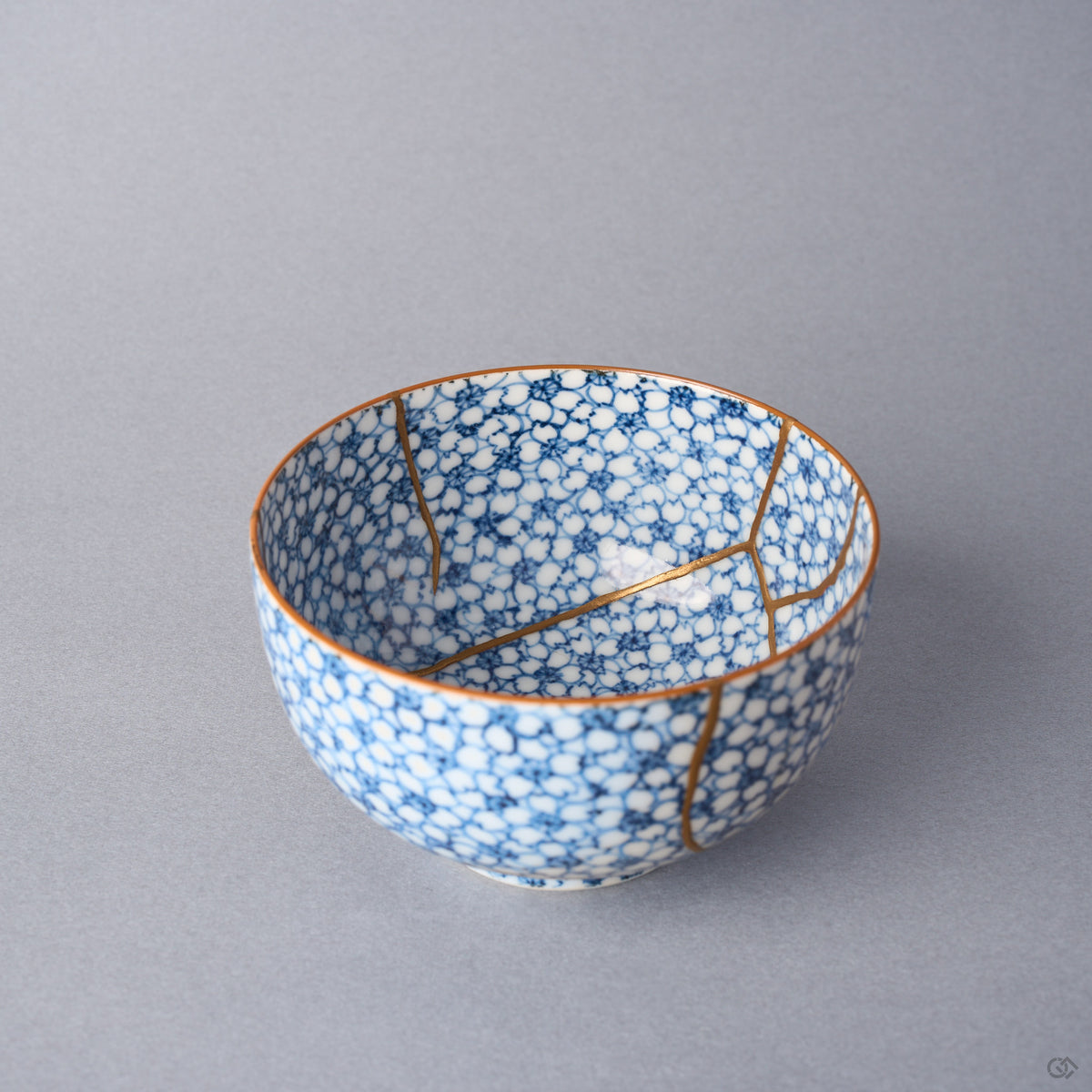 Kintsugi tea cup interior at an angle, urushi and 24K gold lines meeting the rim across the cherry-blossom pattern.