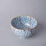 Kintsugi tea cup viewed over the rim, one urushi and 24K gold seam descending into the well beside a second line on the wall.