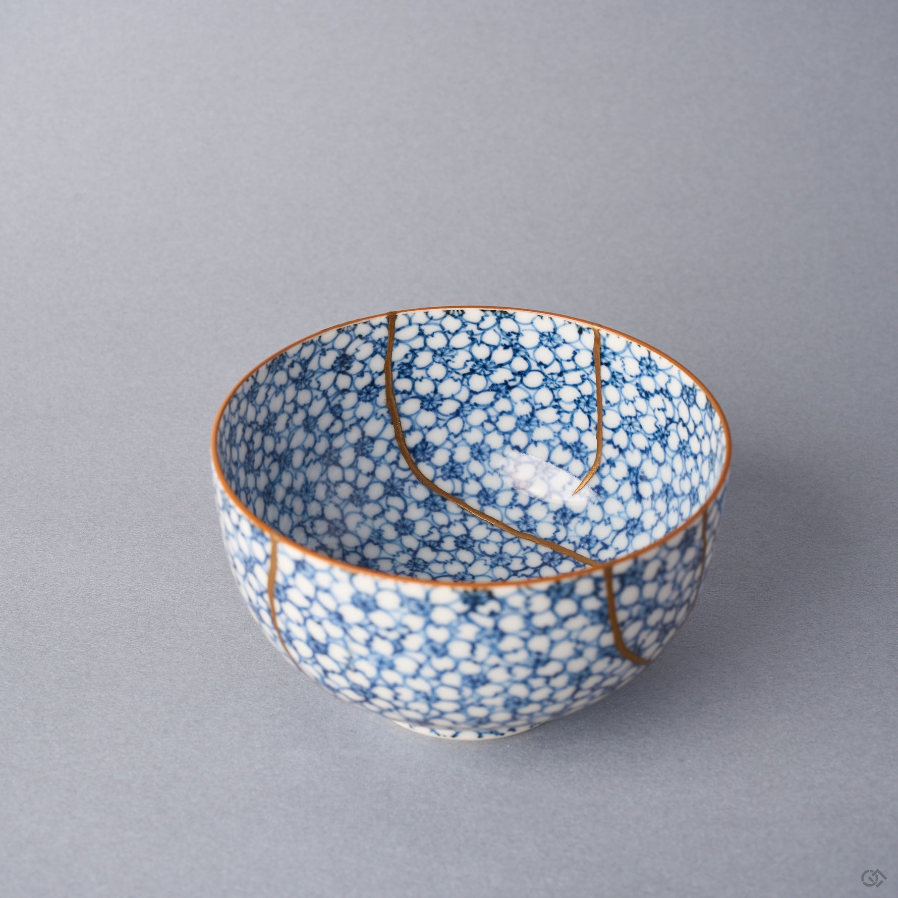 Kintsugi tea cup viewed over the rim, one urushi and 24K gold seam descending into the well beside a second line on the wall.