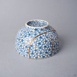 Kintsugi tea cup inverted: urushi and 24K gold lines converge near the foot of the blossom-covered porcelain.