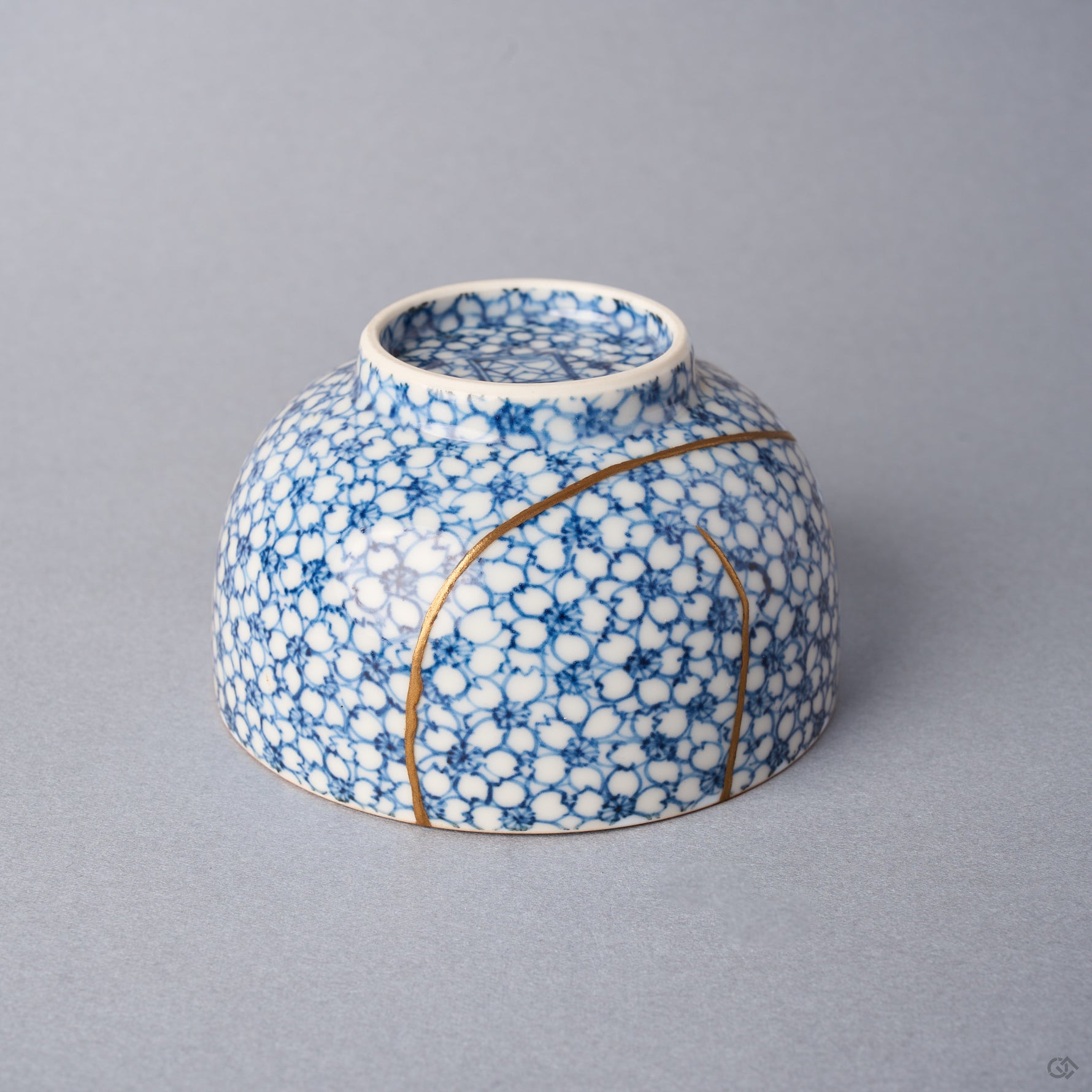 Kintsugi tea cup inverted: urushi and 24K gold lines converge near the foot of the blossom-covered porcelain.