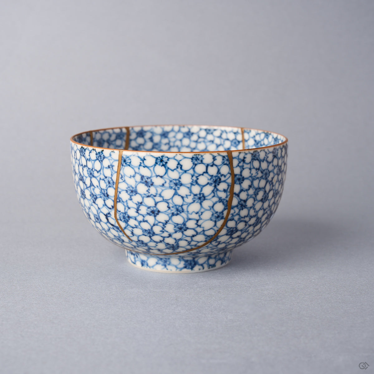 Kintsugi tea cup side view: two urushi and 24K gold lines descend the cherry-blossom wall from the iron-brown rim.