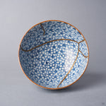 Kintsugi tea cup seen from above; an urushi and 24K gold seam crosses the blossom-covered interior and branches toward the rim.