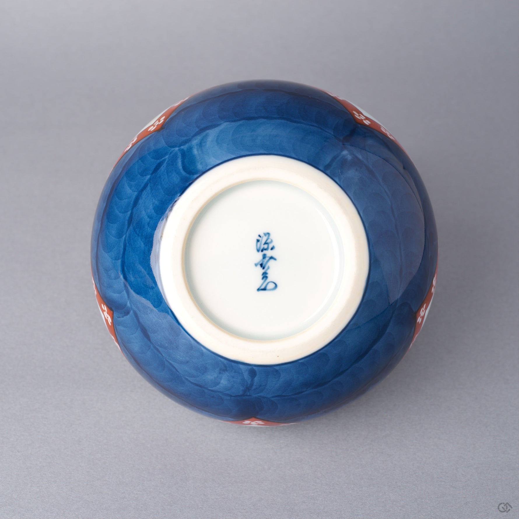 Base of an Arita ware lidded bowl in cobalt-blue porcelain with a white foot ring and a hand-painted cobalt kiln mark, showing the underside of the vessel.