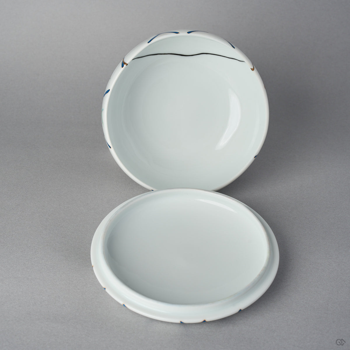 Lid underside and open body of the kintsugi Arita lidded bowl, plain white porcelain interiors with the black urushi restoration line visible inside the bowl near the rim.
