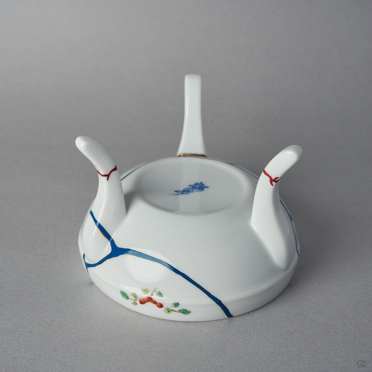 Close-up of iro-urushitsugi on the legs of a kintsugi Arita lidded bowl: vermilion colored urushi sealing the restored feet of the white porcelain tripod, polished to a roiro finish.