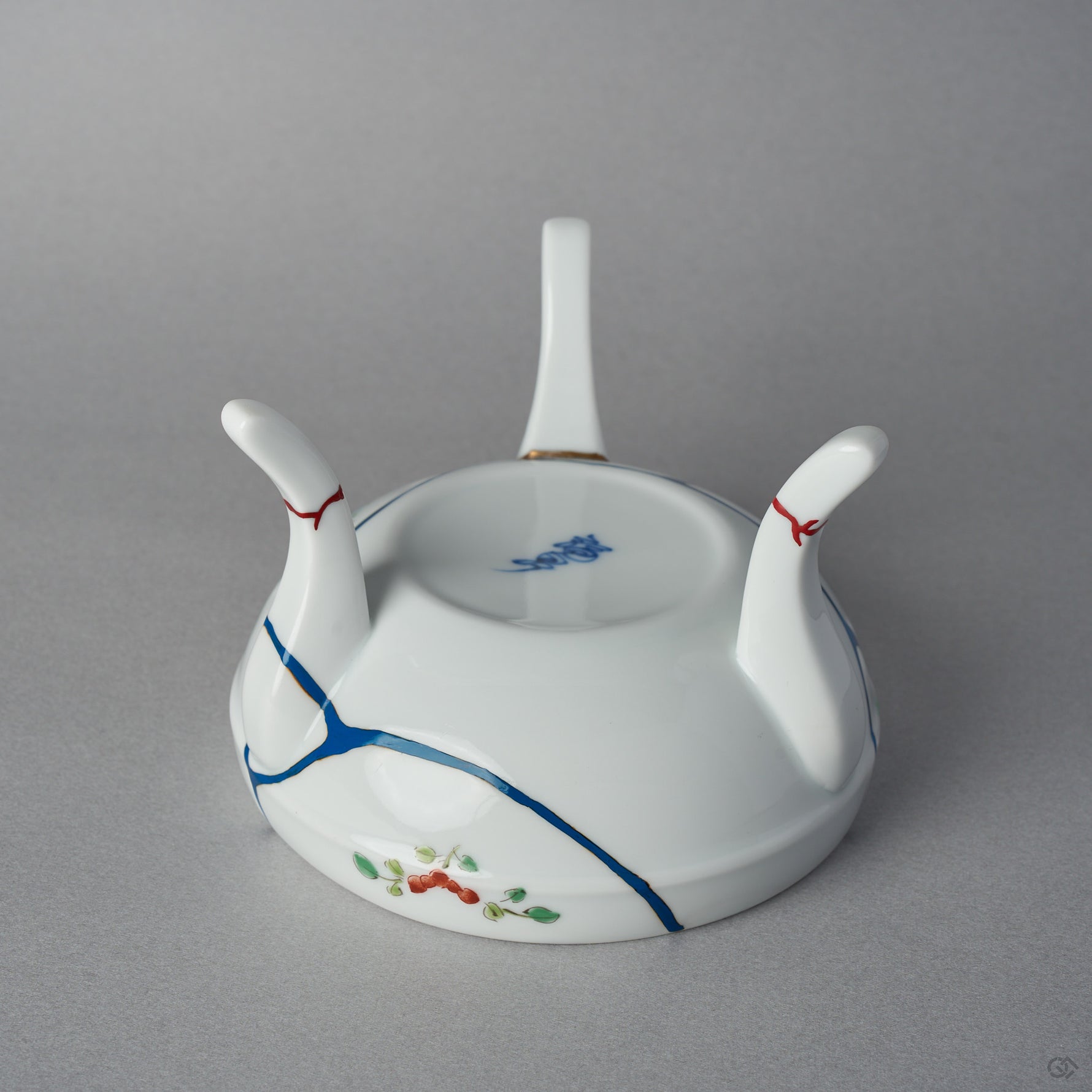 Close-up of iro-urushitsugi on the legs of a kintsugi Arita lidded bowl: vermilion colored urushi sealing the restored feet of the white porcelain tripod, polished to a roiro finish.