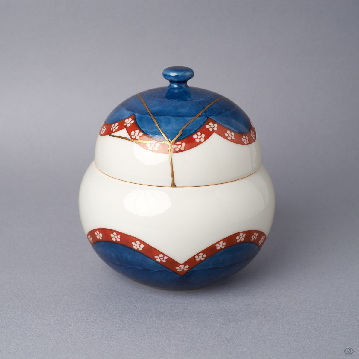 Arita ware lidded bowl in glossy white porcelain with a cobalt-blue domed lid, vermilion plum-blossom bands, and a branching 24K gold kintsugi seam over the crown, shown from the front.