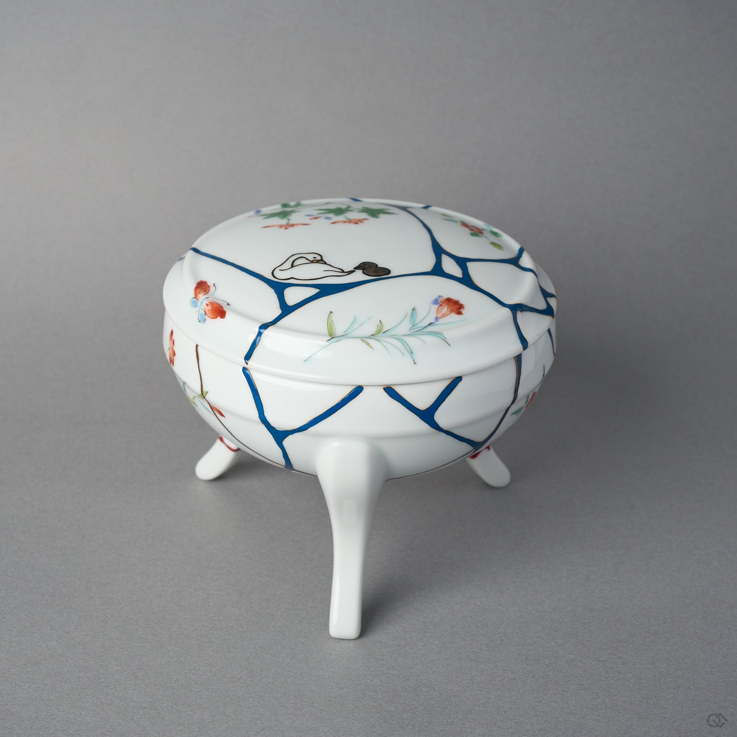 Front view of an Arita ware lidded bowl on three feet, white porcelain with painted flowers and butterflies, blue urushi lines, 24K gold kintsugi seams, and swan maki-e on the lid.