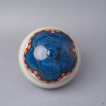 Top view of an Arita ware lidded bowl with the lid in place, a cobalt-blue crown ringed by a vermilion plum-blossom band and a 24K gold kintsugi seam crossing the dome to the knob.